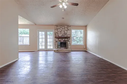 an empty room with wooden floor fireplace and windows