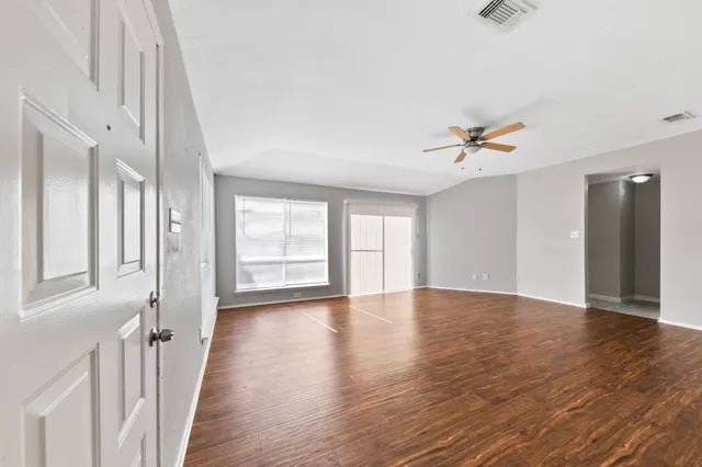 a view of an empty room with wooden floor and a window