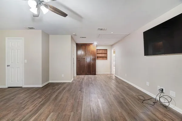 a view of an empty room with wooden floor and a kitchen