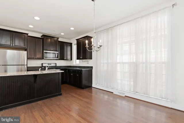 a kitchen with stainless steel appliances granite countertop a refrigerator a sink dishwasher a stove and white cabinets with wooden floor