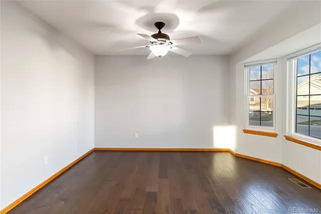 an empty room with wooden floor chandelier fan and windows