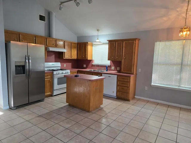 a kitchen with stainless steel appliances granite countertop a stove a sink a refrigerator a window and white cabinets