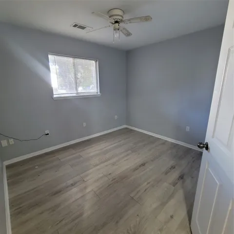 an empty room with wooden floor ceiling fan and windows