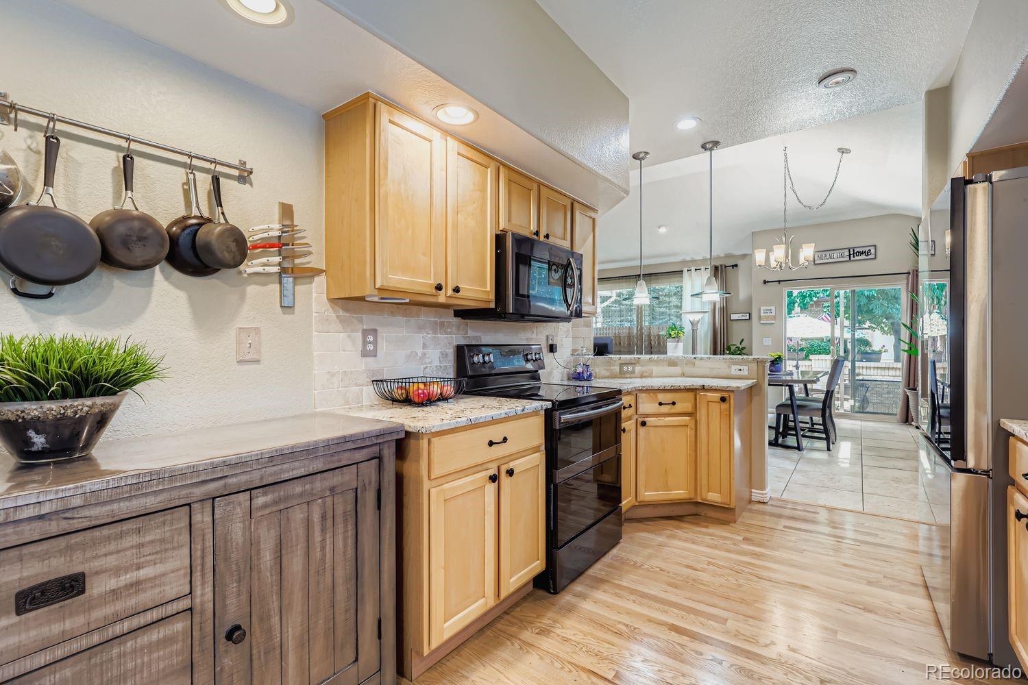 10752 Zuni Drive Denver, CO 80234 - Photo 10 of 27 a kitchen with stainless steel appliances a sink a stove a refrigerator cabinets and a dining table with wooden floor