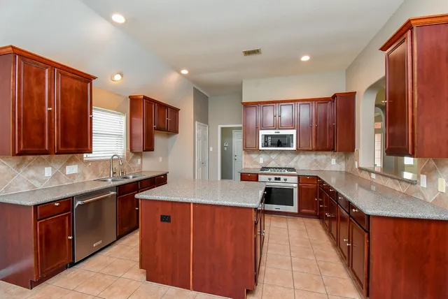 a kitchen with stainless steel appliances granite countertop wooden cabinets a sink dishwasher a stove top oven a refrigerator and dishwasher