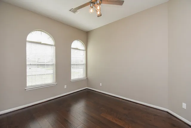 an empty room with wooden floor chandelier and windows