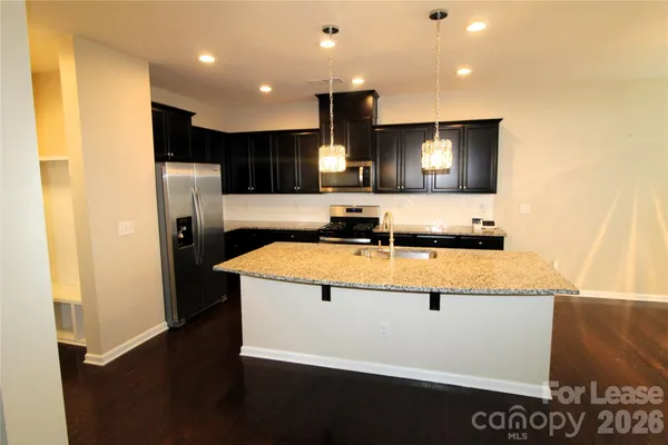 a view of kitchen with stainless steel appliances wooden floor and living room view