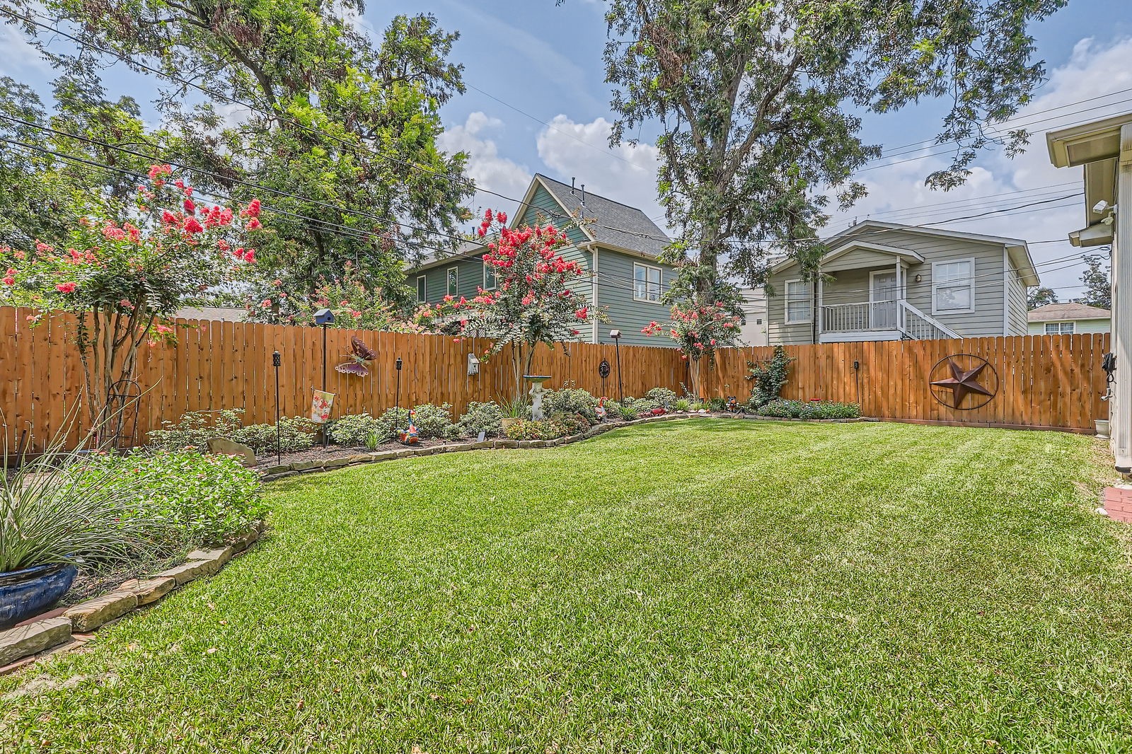 806 East 29th Street Houston, TX 77009 - Photo 24 of 30 Charming backyard with a well-maintained lawn, surrounded by a wooden fence adorned with decorative elements. Mature trees and vibrant flowering plants create a serene atmosphere, perfect for relaxation and outdoor activities.