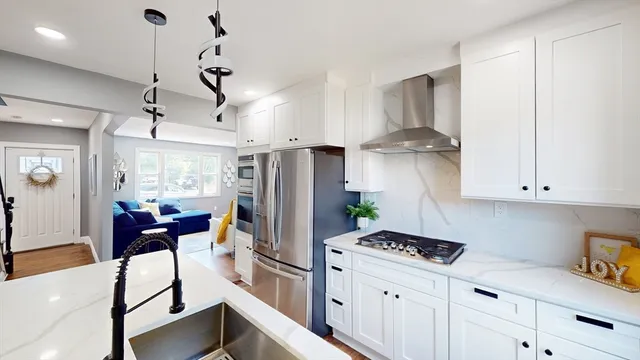 a kitchen with stainless steel appliances kitchen island granite countertop a refrigerator a stove a dining table and chairs with wooden floor