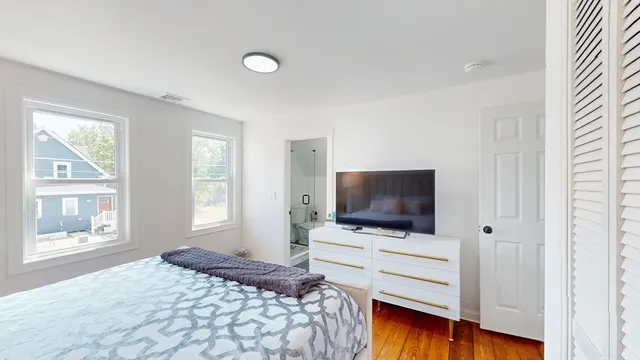 a bedroom with a flat screen tv on dresser and a window