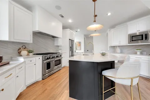 a kitchen with stainless steel appliances a sink a stove a refrigerator cabinets and chairs