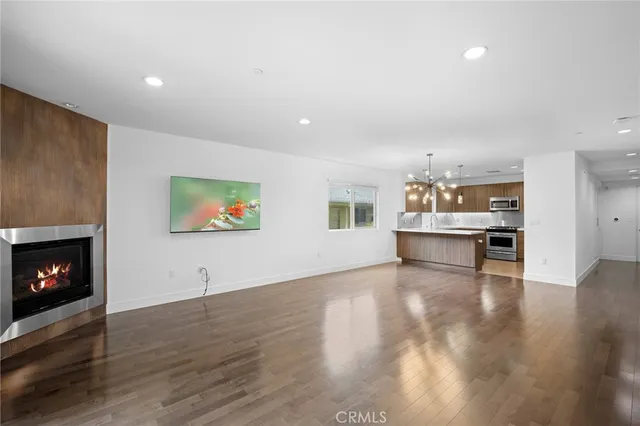 a view of an empty room with wooden floor fire place and a kitchen