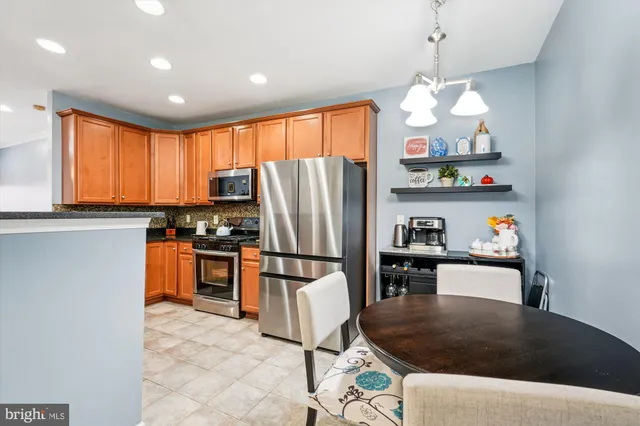 a kitchen with stainless steel appliances granite countertop a refrigerator a stove top oven a sink a dining table and chairs with wooden floor