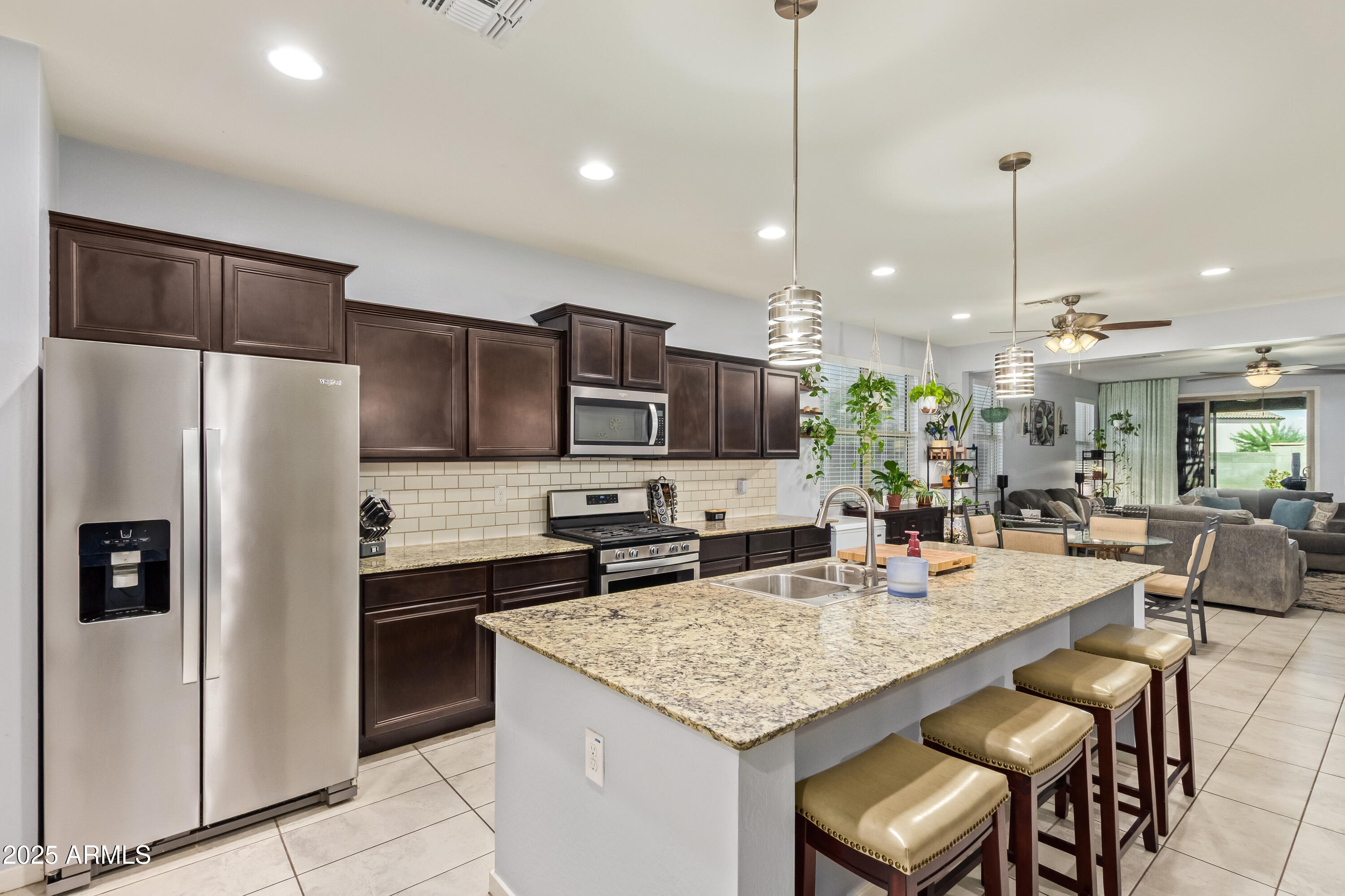 a kitchen with stainless steel appliances kitchen island granite countertop a refrigerator a stove a sink a dining table and chairs with wooden floor