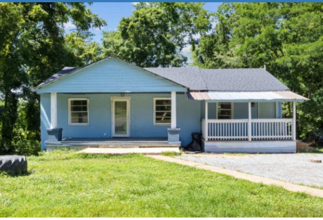 a view of a house with a yard plants and large tree
