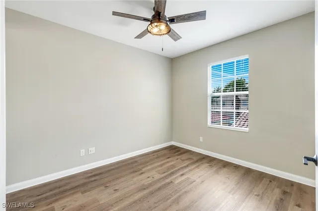 an empty room with wooden floor ceiling fan and windows