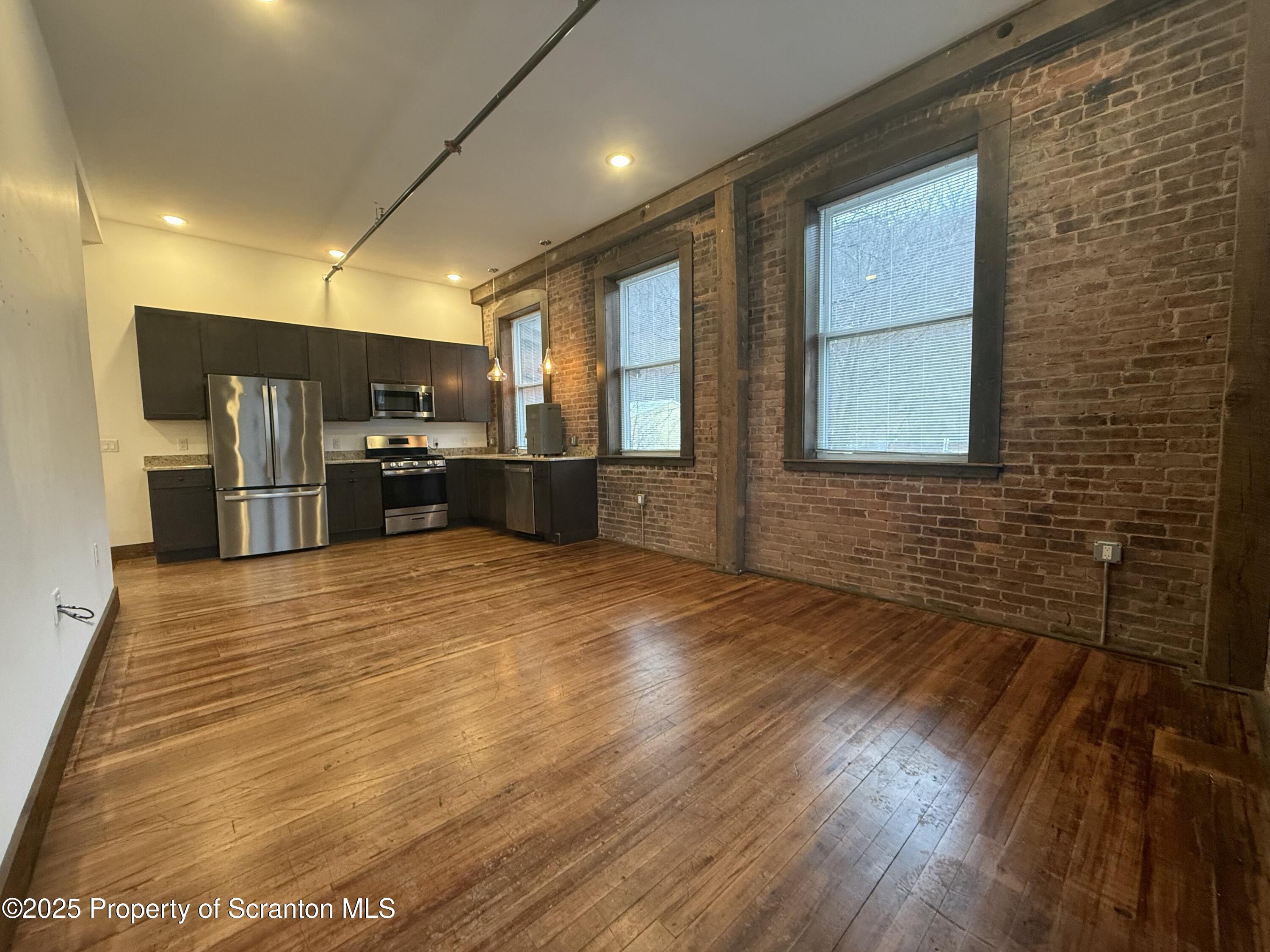 a large room with stainless steel appliances kitchen island granite countertop a refrigerator a sink dishwasher with a dining table and wooden floor