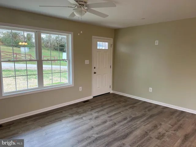 an empty room with wooden floor fan and windows