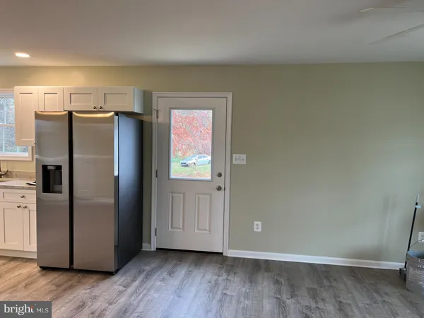 a view of a refrigerator in kitchen and an empty room in wooden floor