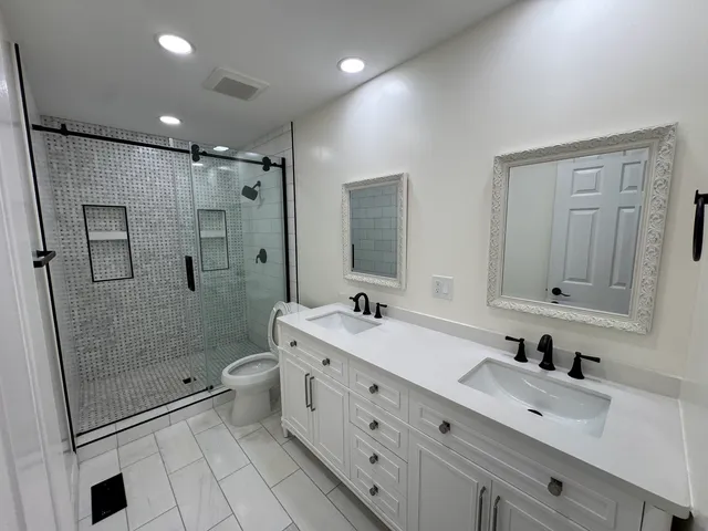 a bathroom with a double vanity sink toilet mirror and shower