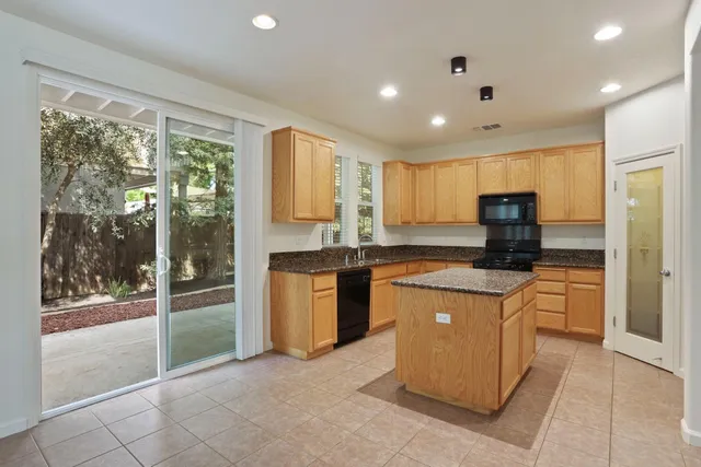 a kitchen with stainless steel appliances granite countertop a refrigerator a sink a stove top oven and a view of living room