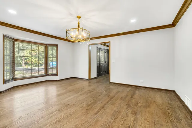 an empty room with wooden floor chandelier and windows