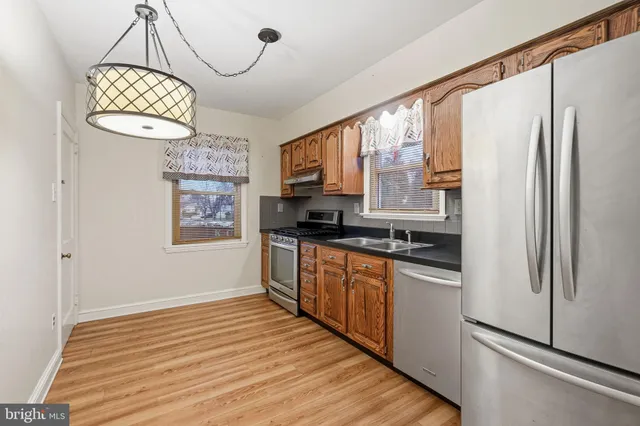 a kitchen with stainless steel appliances granite countertop a refrigerator a sink dishwasher a stove and a dining table with wooden floor