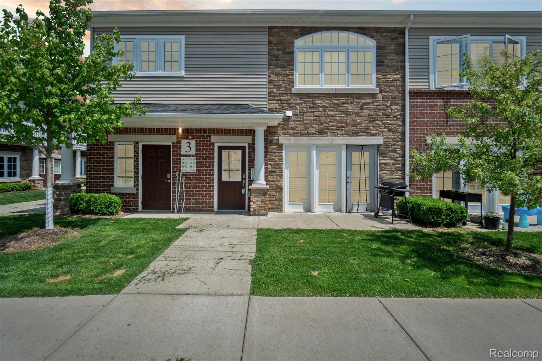 Townhome exterior featuring brick and stone veneer, horizontal siding, multiple entry doors with glass panels, and an arched window on the second level