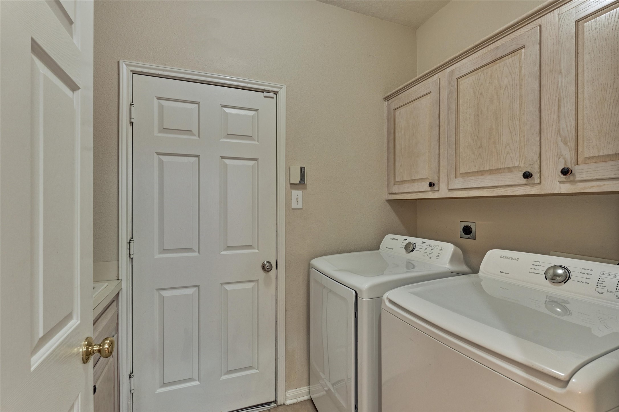 14420 Walters Road, Unit 26 Houston, TX 77014 - Photo 15 of 45 This photo shows a laundry room featuring a washer and dryer set, with upper cabinets for storage and a door leading to garage. The walls are a neutral color, creating a clean and functional area.