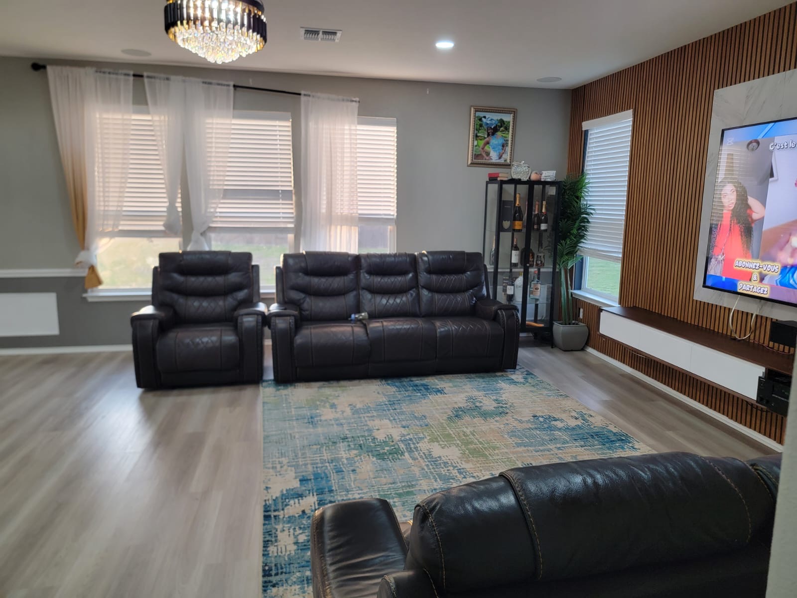 429 Unforgiven Lane Jarrell, TX 76537 - Photo 6 of 10 Spacious living area featuring light wood-finish flooring, a contemporary chandelier, multiple windows with horizontal blinds, a custom wood-slat accent wall, and a built-in media console