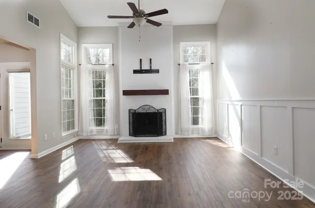 a view of a livingroom with wooden floor a ceiling fan and windows