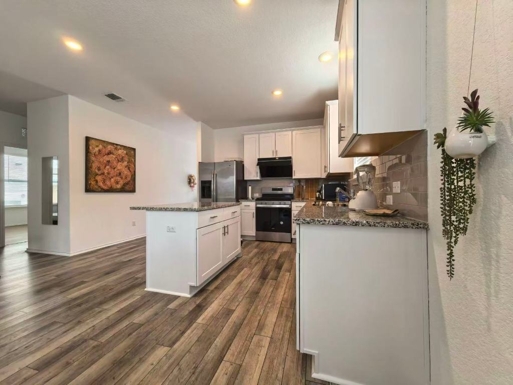 1521 Hope Rnch Road Leander, TX 78641 - Photo 6 of 15 Kitchen featuring appliances with stainless steel finishes, white cabinetry, a kitchen island, dark stone counters, and dark wood-style flooring