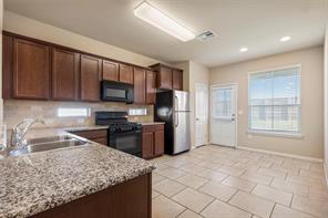 407 Epiphany Lane Pflugerville, TX 78660 - Photo 4 of 29 Kitchen with black appliances, dark wood finish cabinets, recessed lighting, and light tile patterned flooring
