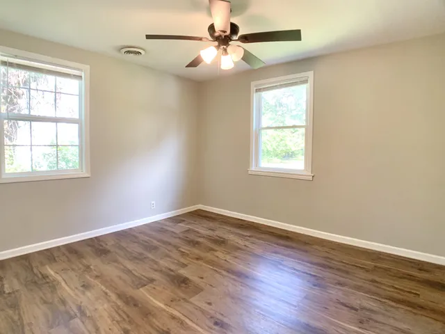 an empty room with wooden floor windows and fan