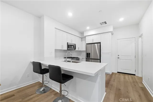 a kitchen with stainless steel appliances a stove a refrigerator white cabinets and wooden floor