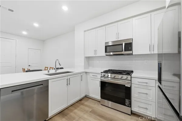 a kitchen with cabinets stainless steel appliances a sink and a stove with wooden floor