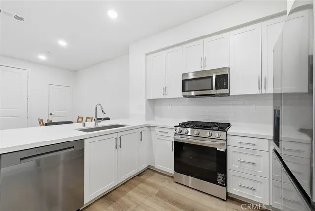 a kitchen with cabinets stainless steel appliances a sink and a stove with wooden floor