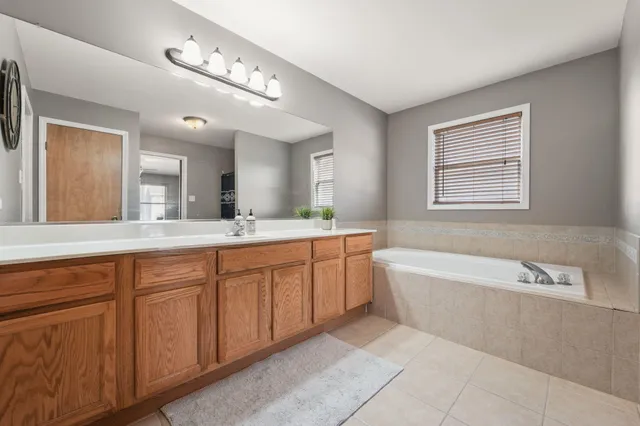 a spacious bathroom with a double vanity sink a mirror a bathtub and next to a window