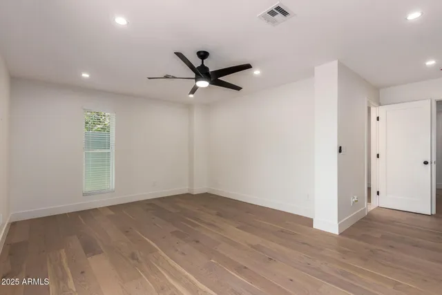 a view of an empty room with wooden floor and a ceiling fan