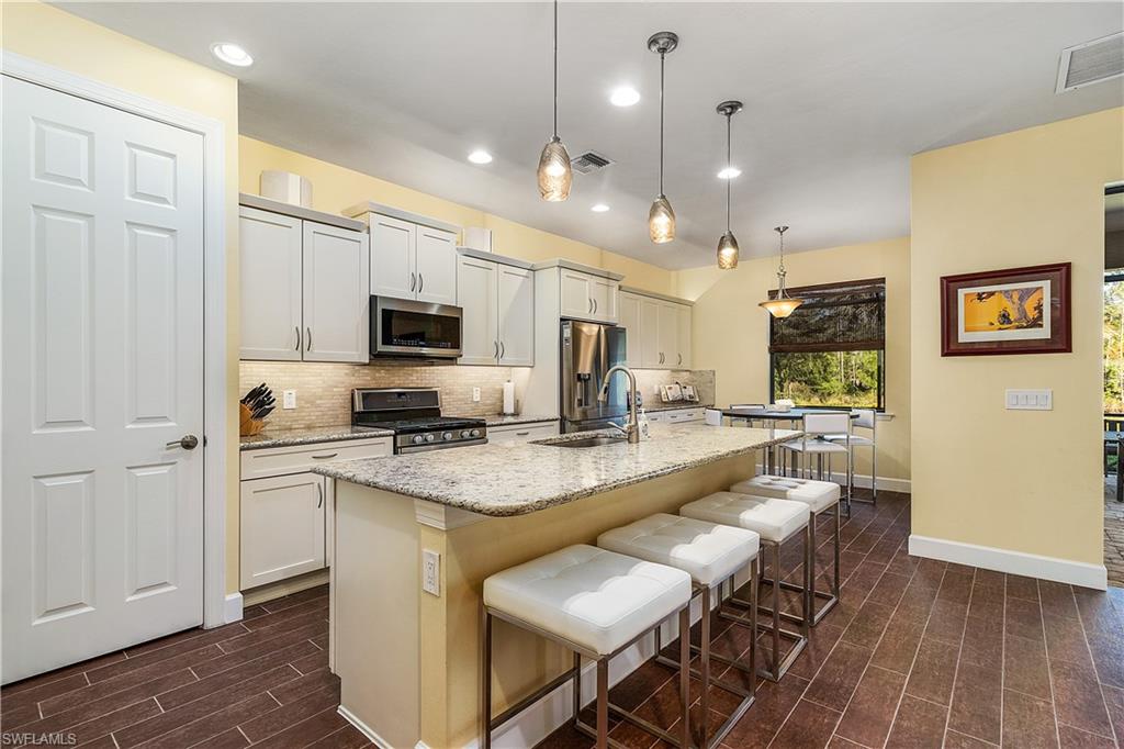 16309 Winfield Lane Naples, FL 34110 - Photo 10 of 35 a kitchen with stainless steel appliances granite countertop a stove top oven a sink dishwasher a dining table and chairs with wooden floor