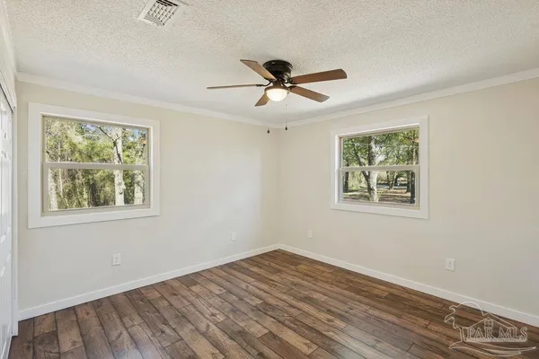 an empty room with wooden floor ceiling fan and windows