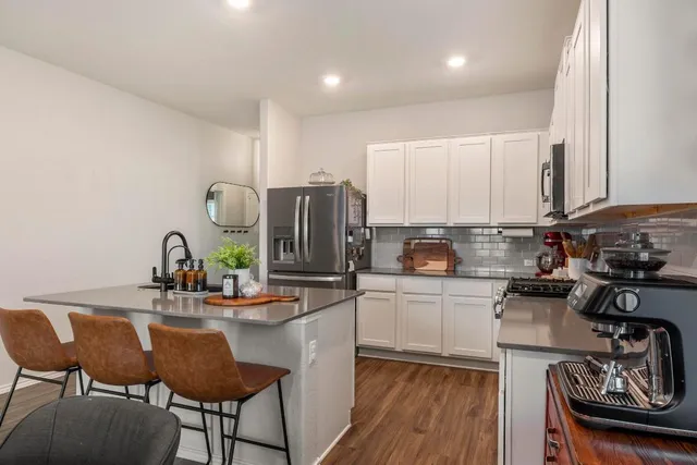 a kitchen with stainless steel appliances granite countertop a stove top oven a refrigerator a sink and chairs