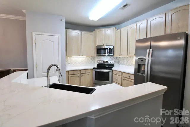 a kitchen with stainless steel appliances a sink a stove top oven a refrigerator with white cabinets and wooden floor