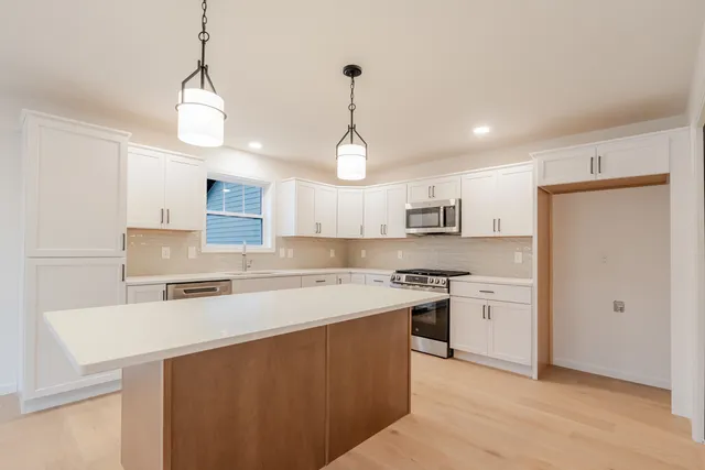 a kitchen with stainless steel appliances granite countertop a sink a stove a refrigerator and white cabinets