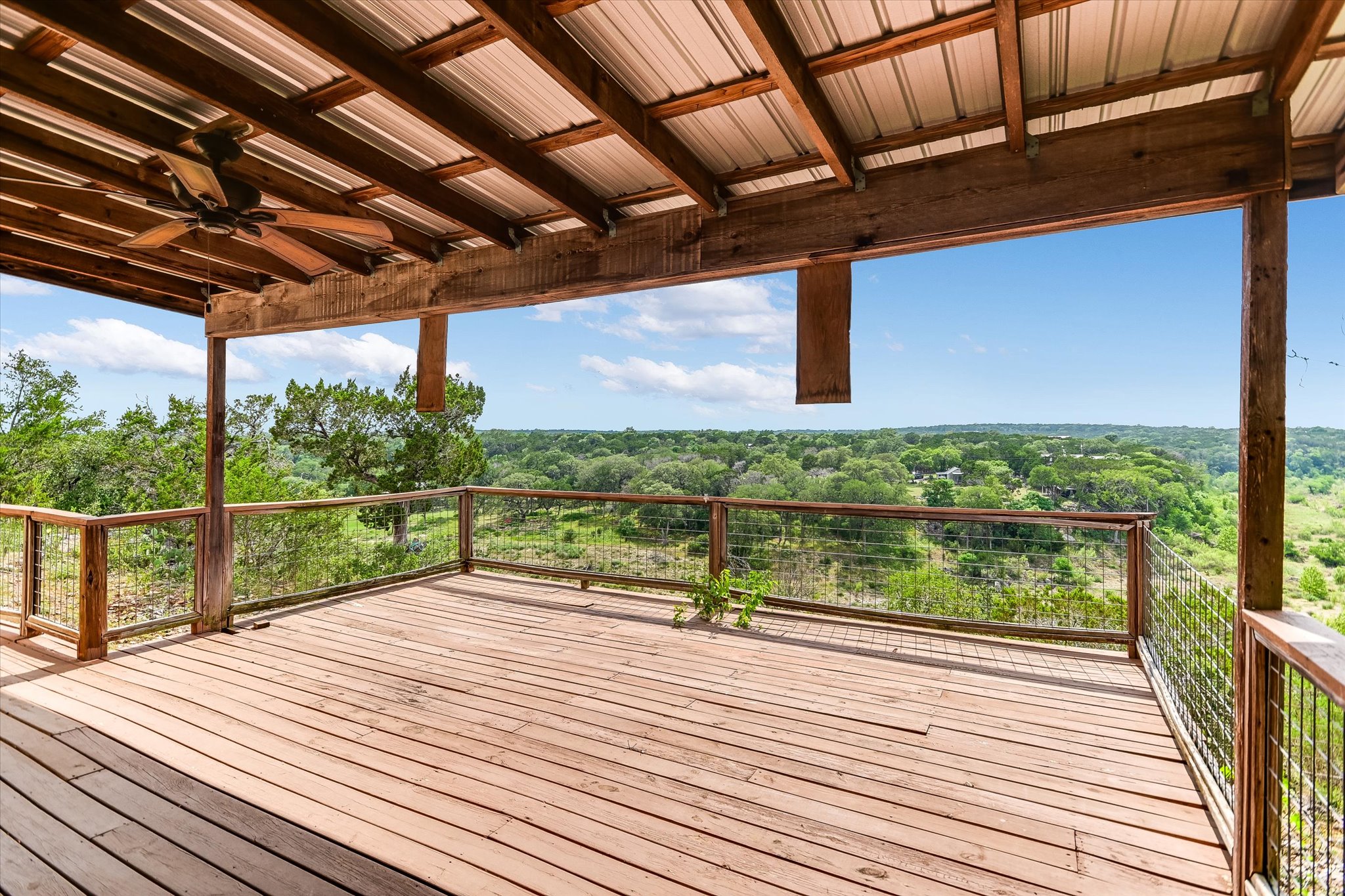 700 Cliffside Road Wimberley, TX 78676 - Photo 11 of 22 Expansive outdoor deck featuring wood-finish flooring, a wood-framed railing with cable infill, and a covered patio with a metal roof