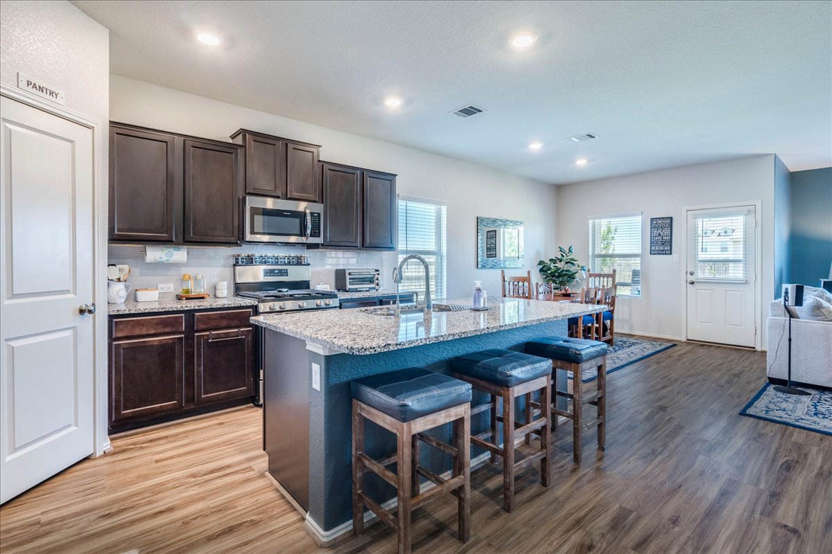 358 Jasper Trail Buda, TX 78610 - Photo 7 of 35 Spacious kitchen featuring an island with granite countertop, dark wood-finish cabinetry & stainless steel appliances.