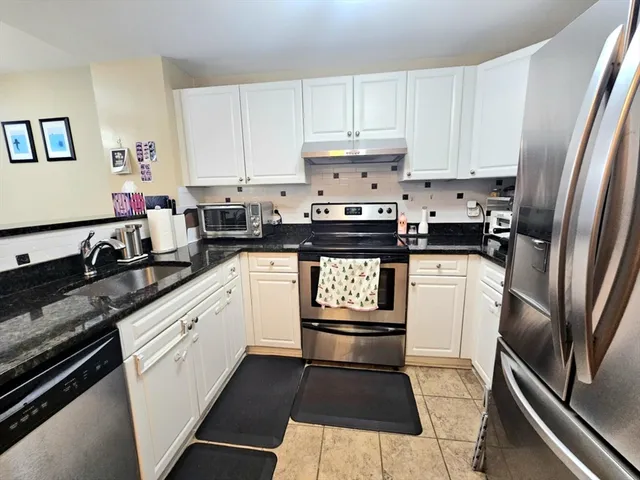 a kitchen with stainless steel appliances granite countertop a refrigerator a sink a stove and white cabinets