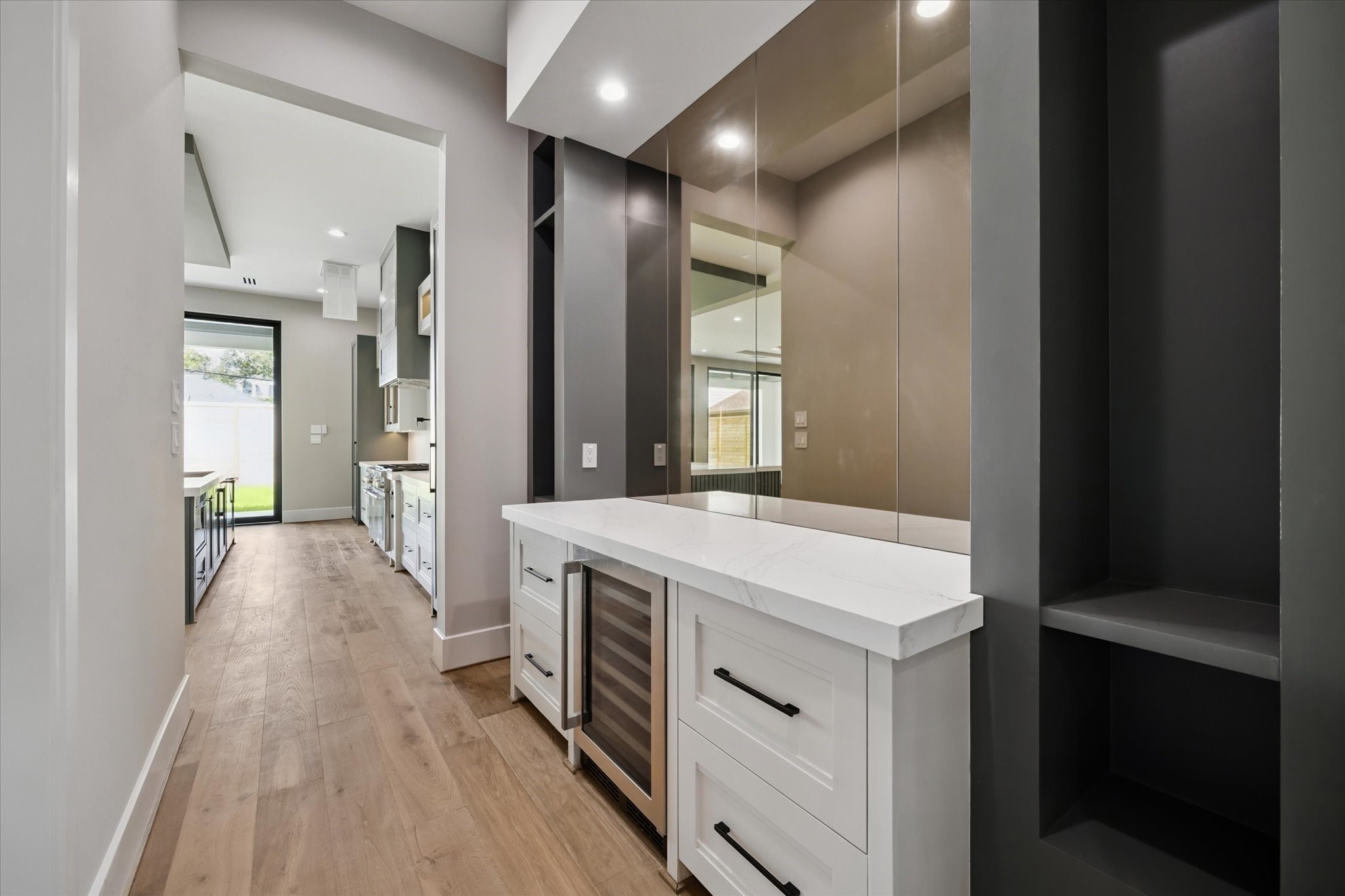 2120 Branard Street Houston, TX 77098 - Photo 12 of 33 The butler’s pantry bar area is both stylish and functional, highlighted by an antiqued mirrored wall that adds depth and sophistication. Inset shelving provides elegant display space, while a sleek quartz buffet with a built-in wine cooler and four drawers offers ample storage and convenience for entertaining.