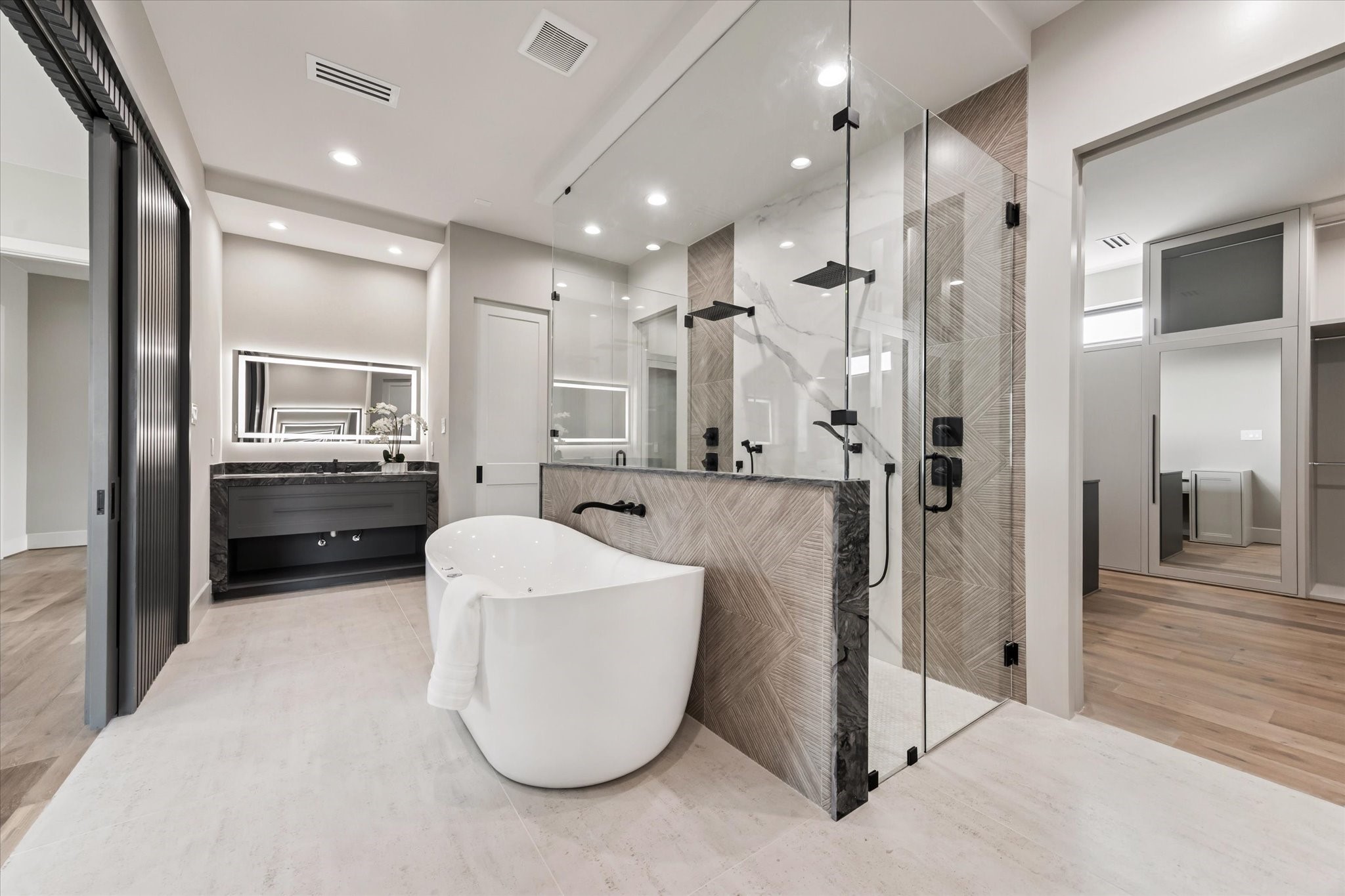 2120 Branard Street Houston, TX 77098 - Photo 17 of 33 This spa-like primary bathroom is designed to impress with its modern elegance and luxurious finishes. At the center, a freestanding soaking tub creates a striking focal point, perfectly framed by a glass-enclosed shower featuring dual rainfall showerheads and dramatic tile detail.