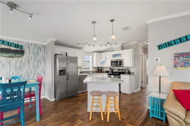 a kitchen with stainless steel appliances kitchen island granite countertop a refrigerator a stove top oven a dining table and chairs with wooden floor
